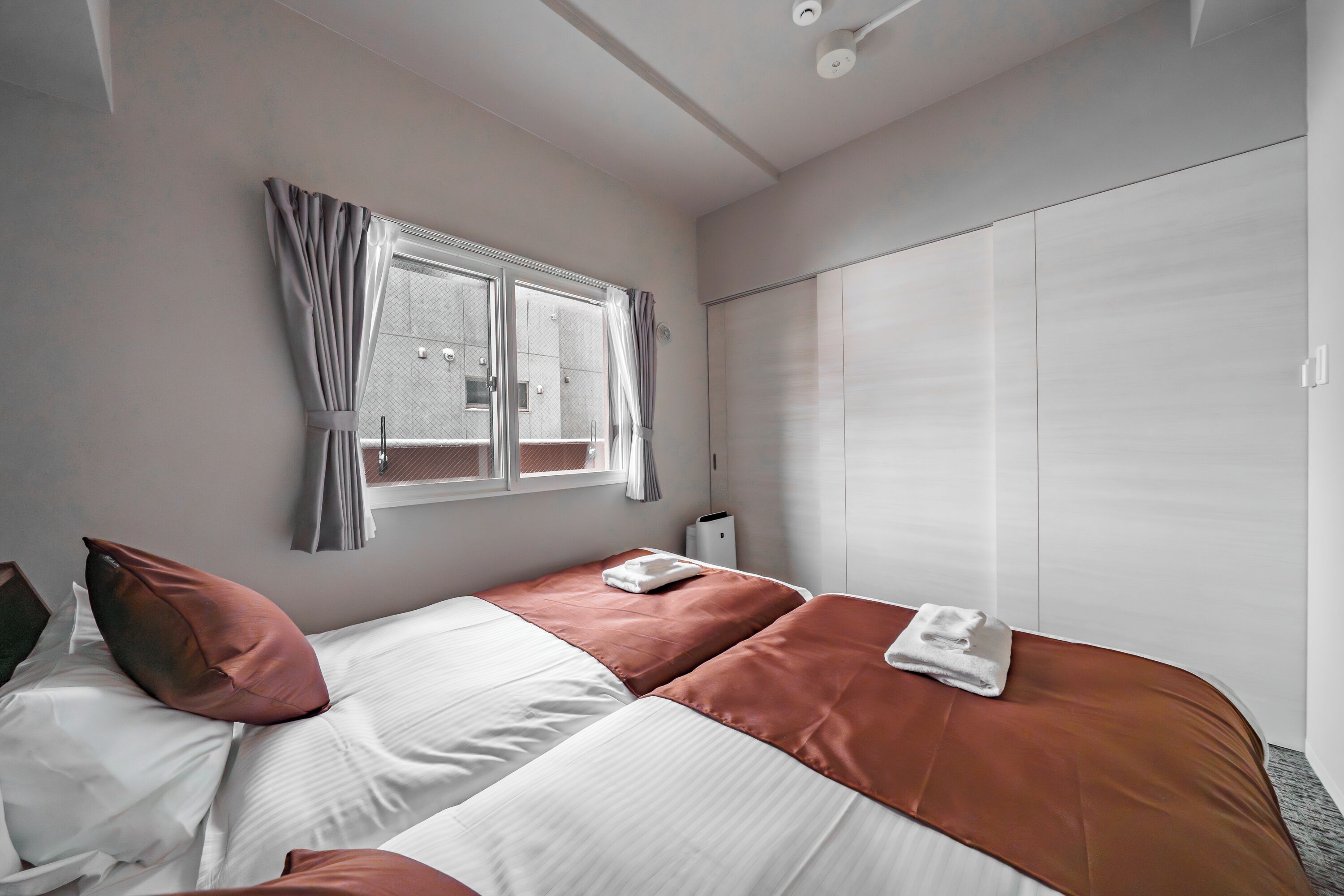 A bedroom with a bed, a window with curtains, a wardrobe, and a bedside table.