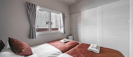 A bedroom with a bed, a window with curtains, a wardrobe, and a bedside table.