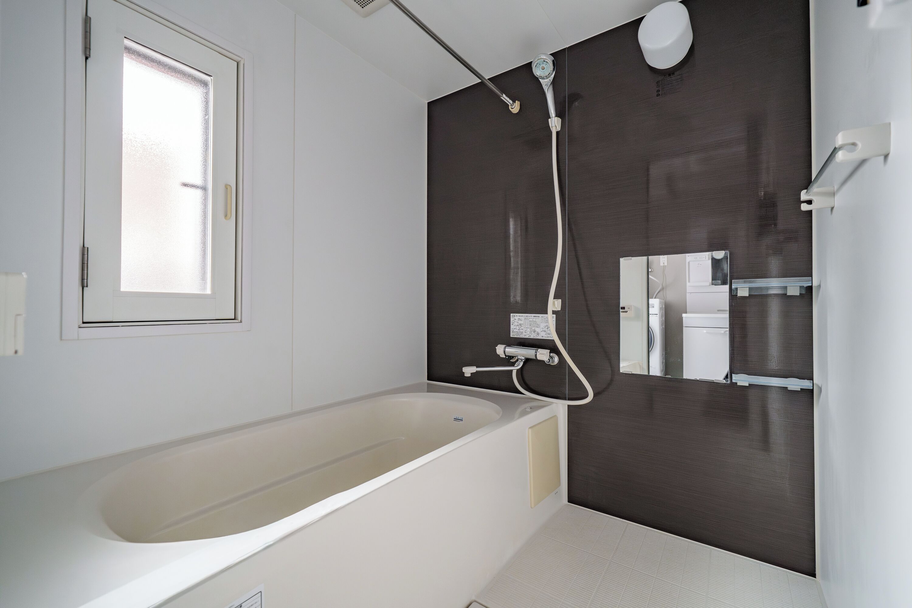 Un baño moderno con una bañera independiente, un cabezal de ducha y un inodoro visibles a través de un separador de vidrio.