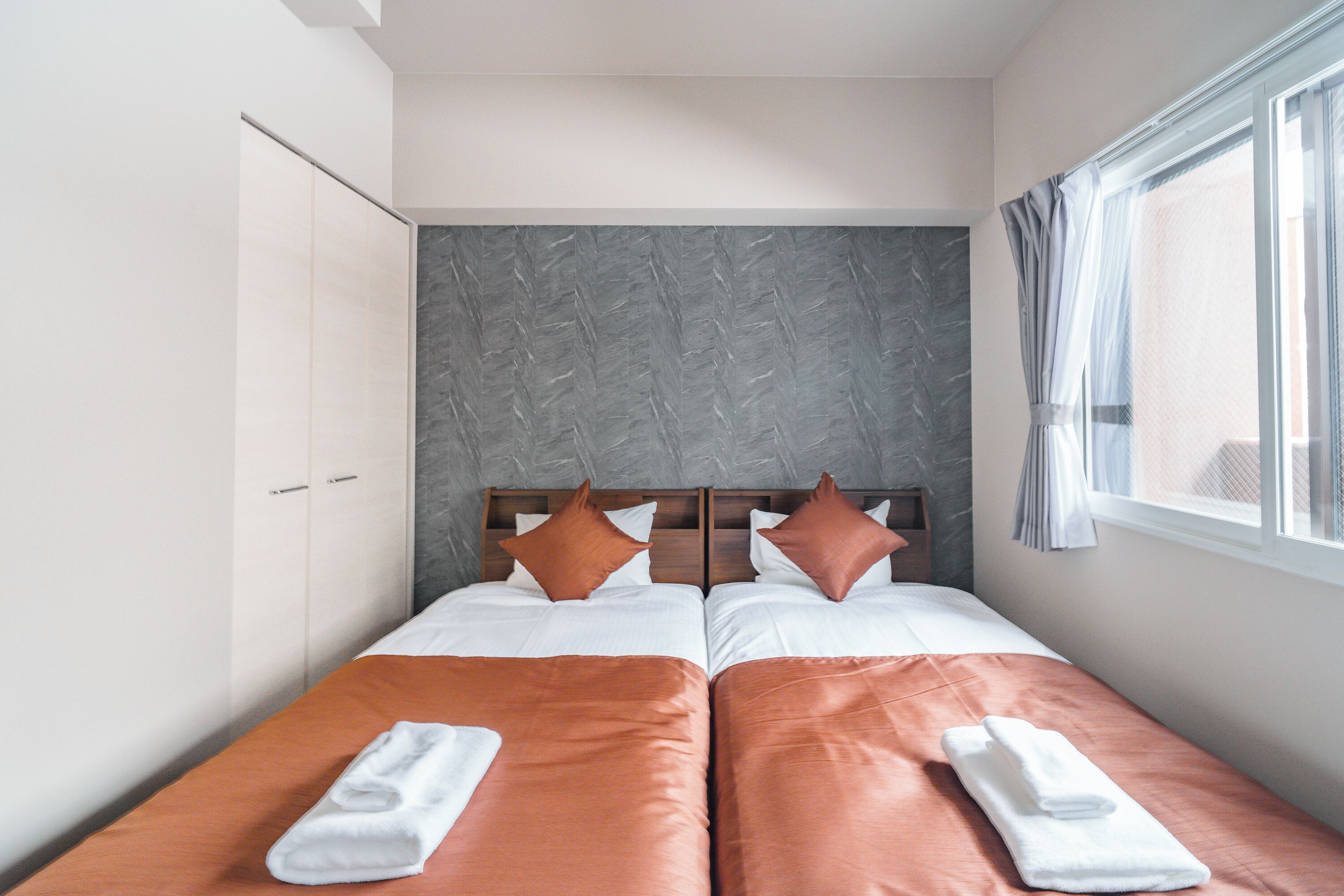 Cama doble con dos almohadas, cabecera de madera y ventana con cortinas.