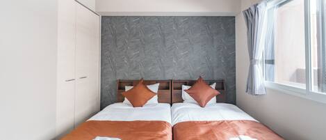 Cama doble con dos almohadas, cabecera de madera y ventana con cortinas.