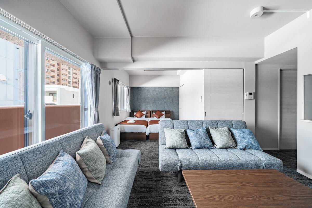A modern hotel room with a large window, a sofa, a bed, and a wooden coffee table.