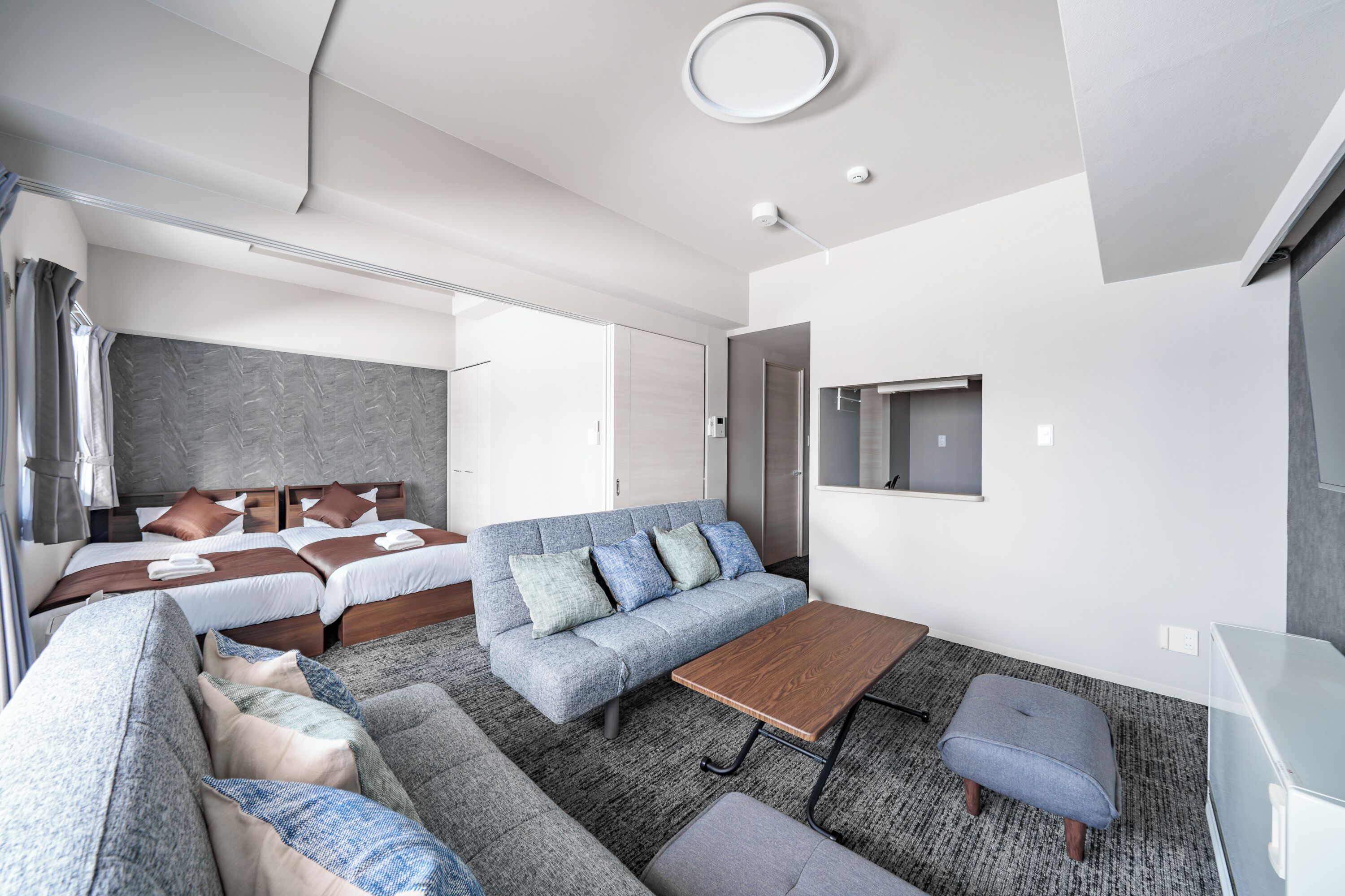 Una habitación de hotel moderna con un sofá, dos camas, una mesa de centro y un televisor.