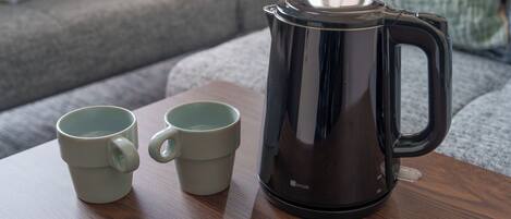 A coffee maker and two mugs on a wooden table in a living room.