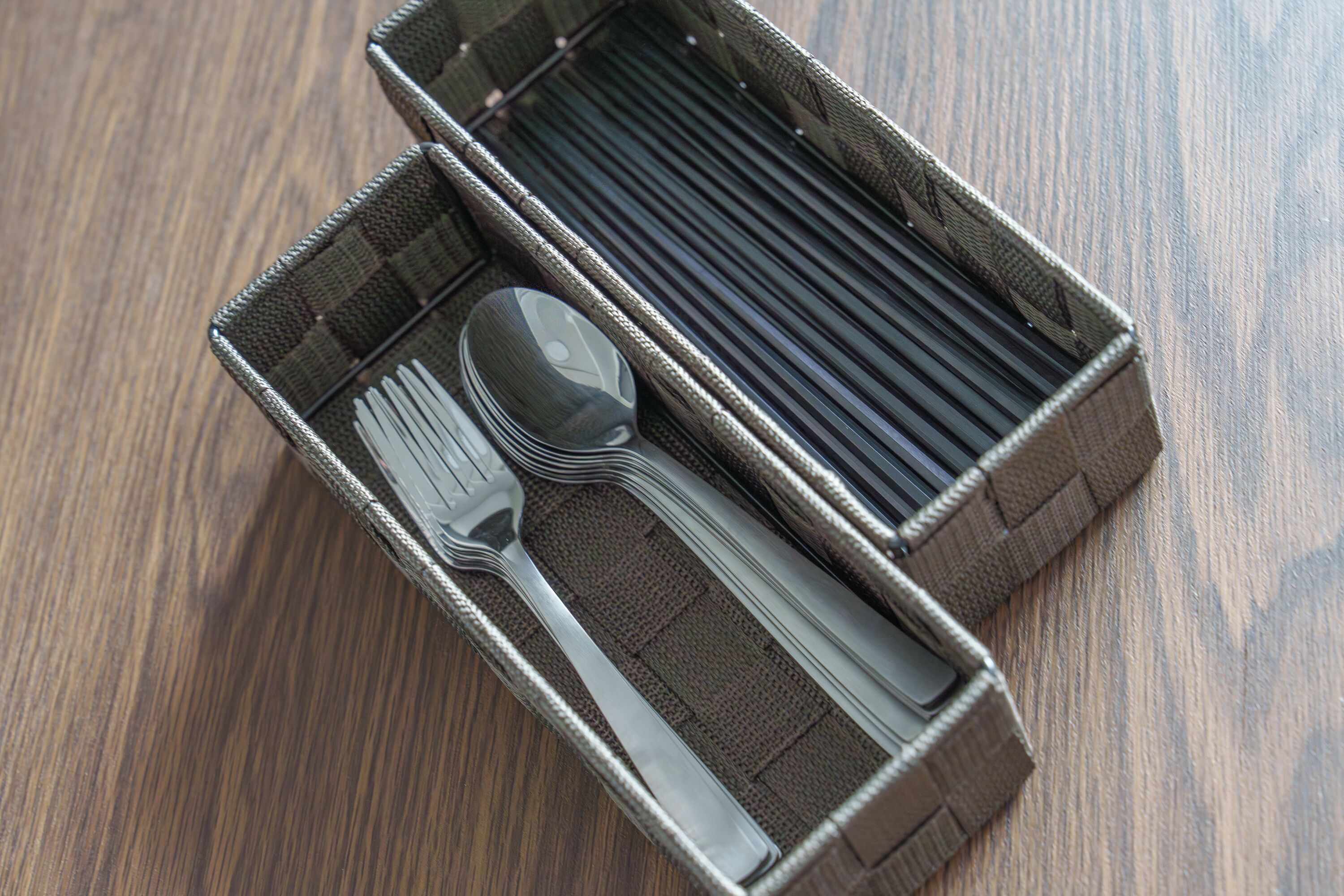 A compact, woven-texture box containing a fork, spoon, and knife.