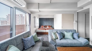 A modern hotel room with a large window, a bed with a headboard, a grey sofa set, and a wooden coffee table. - MP STYLE SAPPORO-50 (Sapporo)