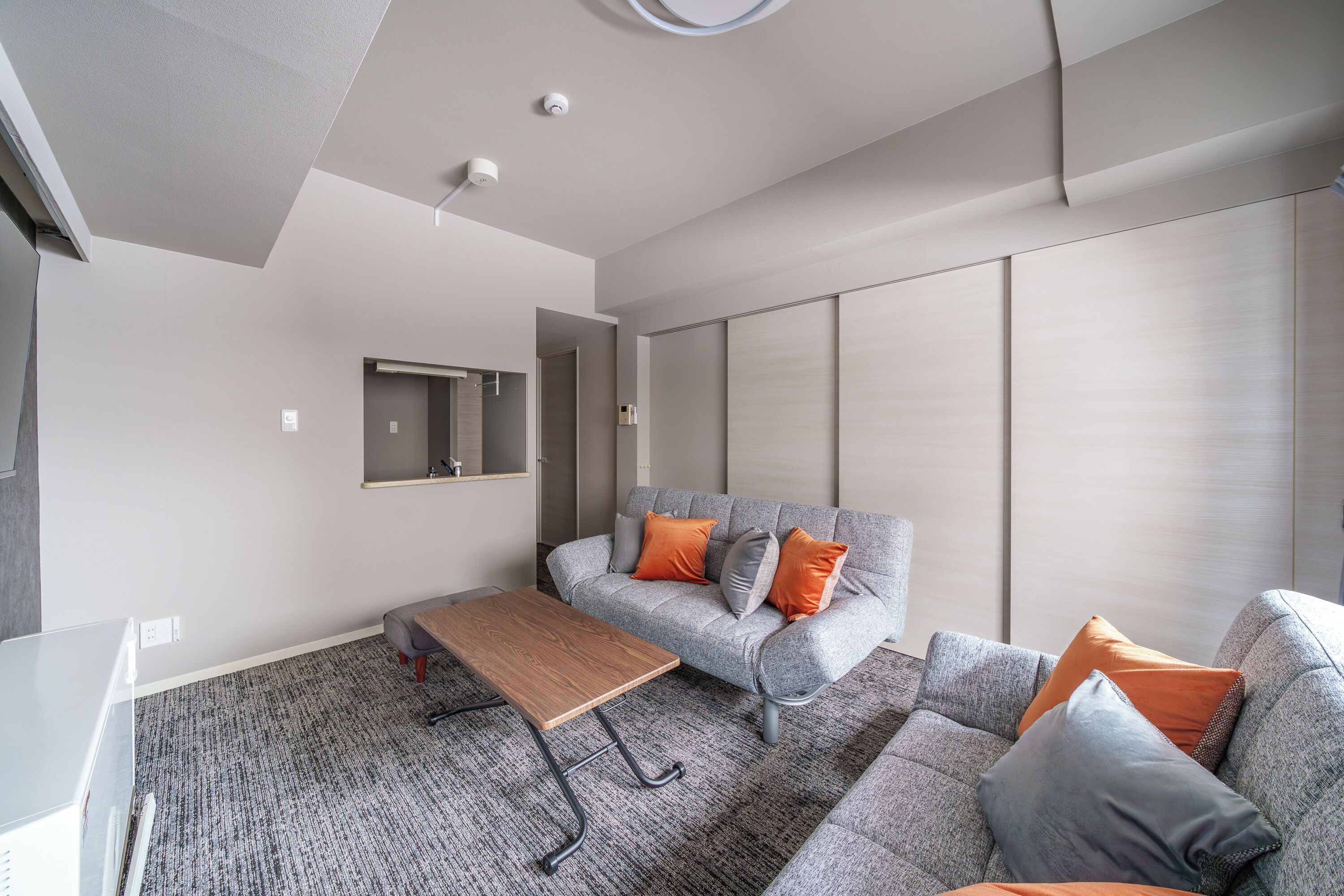 Un salón moderno con un sofá gris, cojines naranja, una mesa de centro de madera y una alfombra gris.