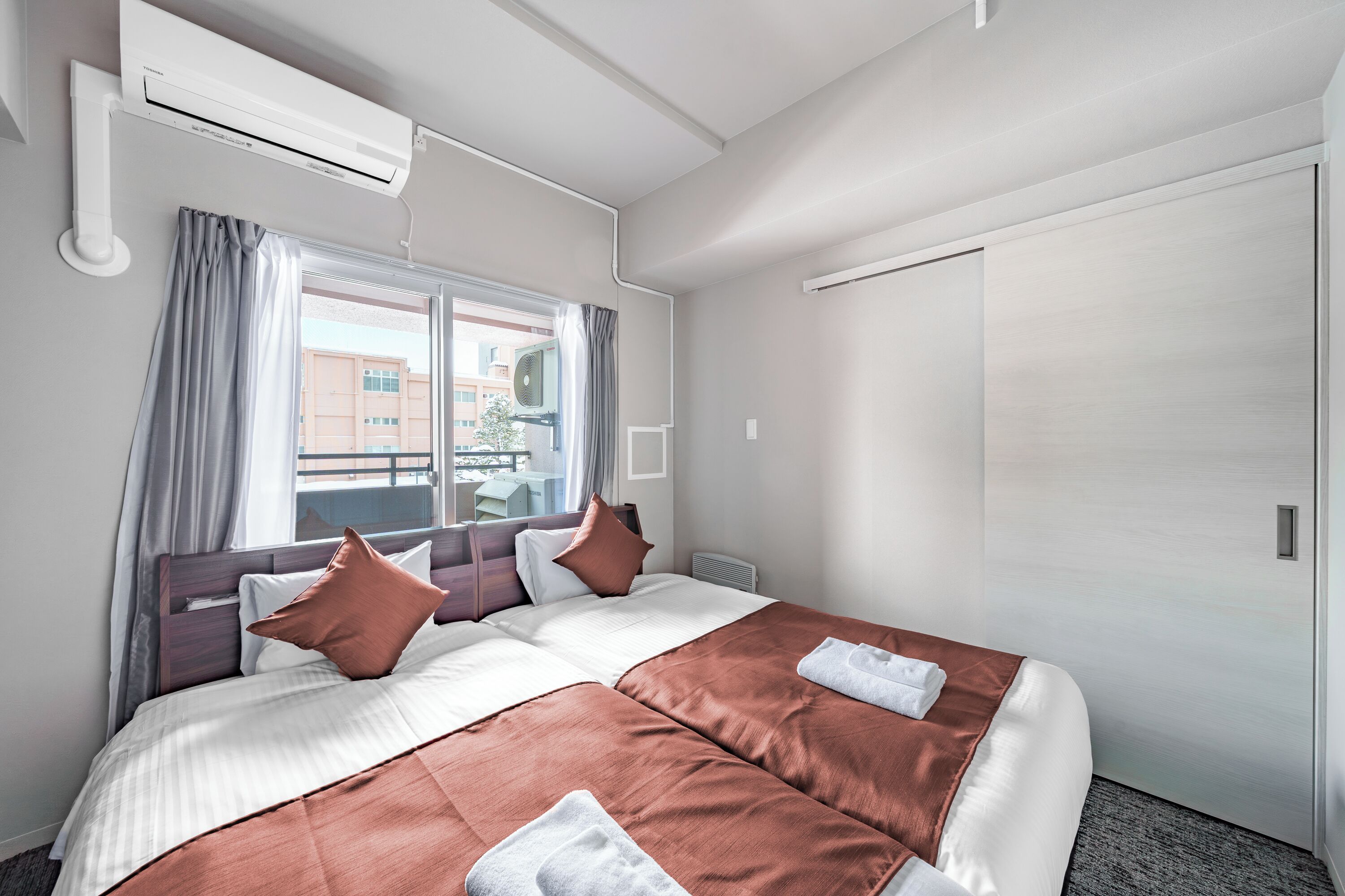 Une chambre d’hôtel avec un grand lit, deux oreillers, une fenêtre avec des rideaux, un appareil de climatisation et une porte.