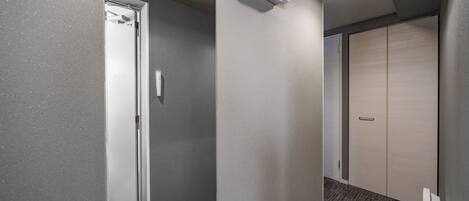 A hallway with a door, a light switch, and a thermostat on the wall.