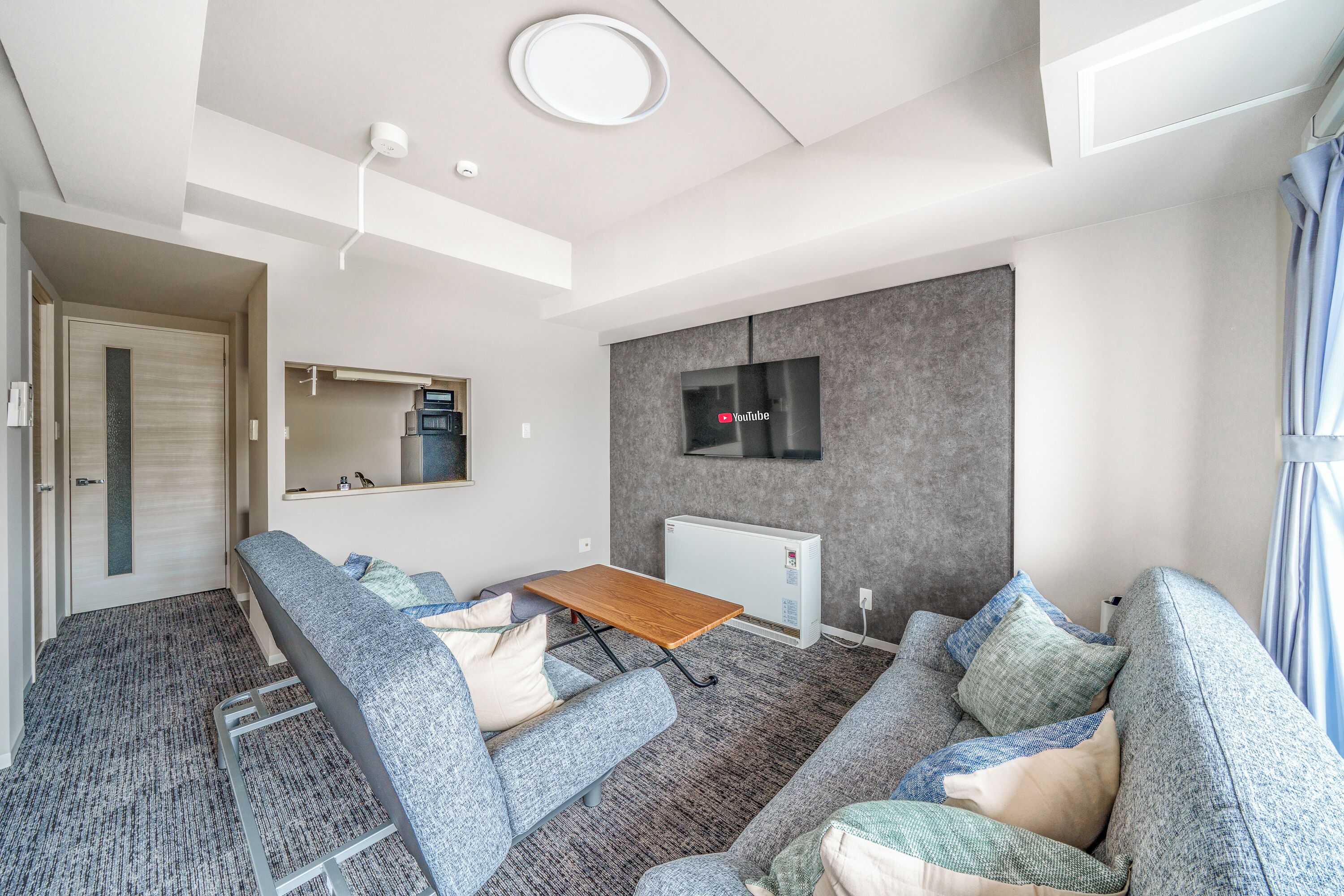 A modern living room with a sofa, a small table, and a TV mounted on the wall.