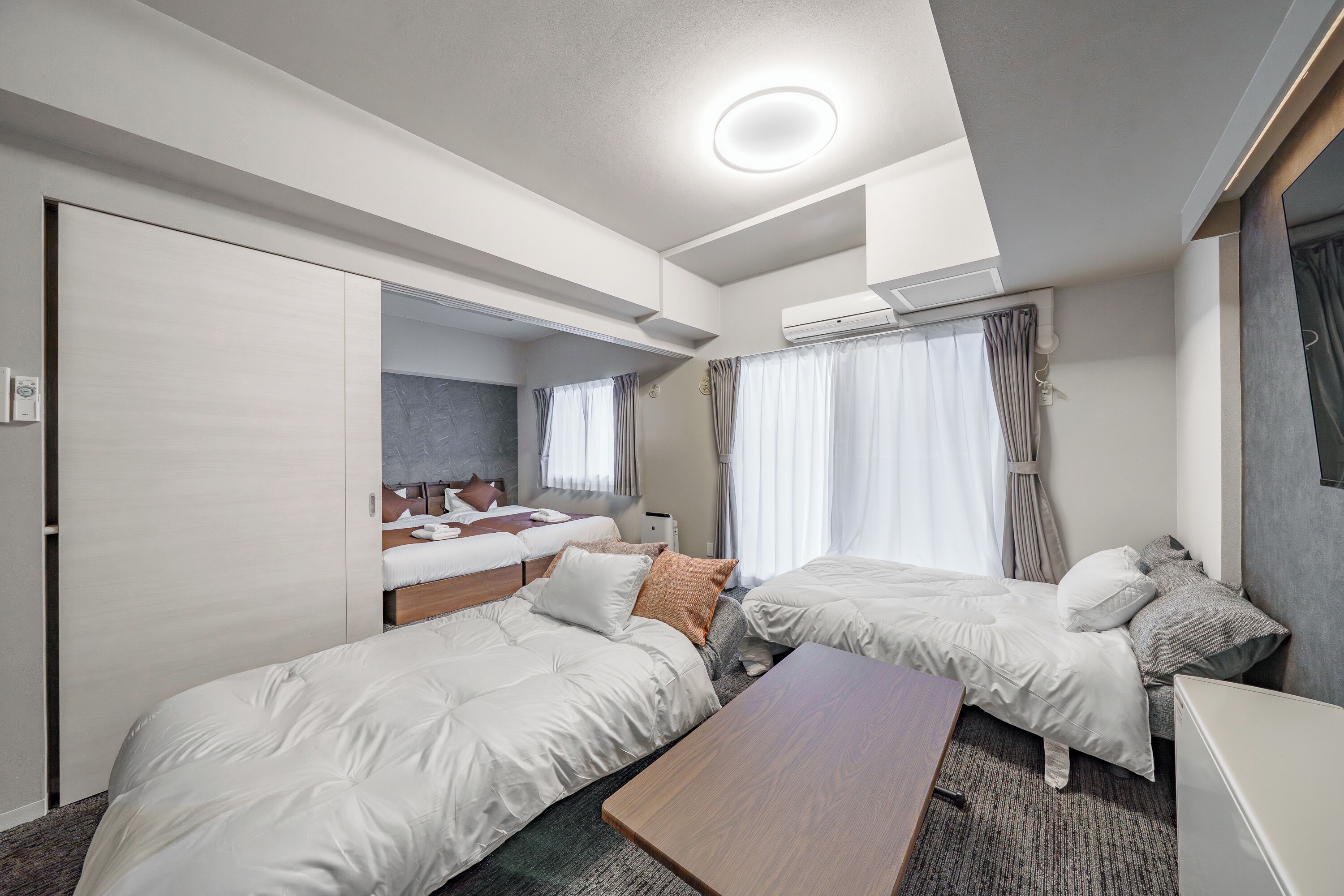 A modern hotel room with two beds, a wooden table, and a built-in wardrobe.