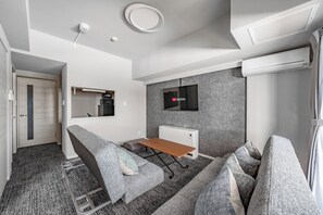 Un espacio habitable moderno y funcional con un sofá gris, una mesita de madera y un televisor montado.