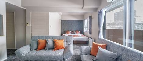 Een moderne hotelkamer met een grijze zithoek, een houten salontafel en een bed met oranje en grijze kussens.