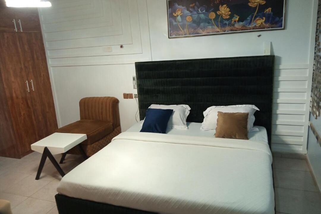 A bedroom with a bed, a nightstand, a wooden wardrobe, and a painting on the wall.