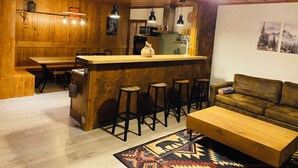 A wooden interior with a bar area, stools, a sofa, and a patterned rug. - Apartment in the heart of the Dessoubre valley (Battenans-Varin)