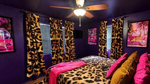 Une chambre à coucher avec une couvre-lit à motifs léopard, un ventilateur de plafond et des rideaux ornés d’un motif léopard.