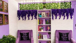 Une pièce avec deux fauteuils violets, une bibliothèque blanche et un mur en briques blanches.