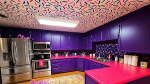 Une cuisine moderne avec des meubles de couleur violette, des appareils électroménagers en acier inoxydable et un tapis abstrait aux couleurs vives.