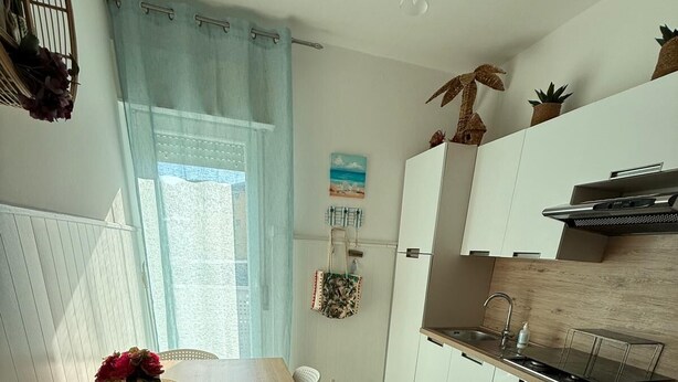 Eine moderne Küche mit weißen Schränken, einer Holzarbeitsplatte und einem Fenster mit hellblauen Vorhängen.