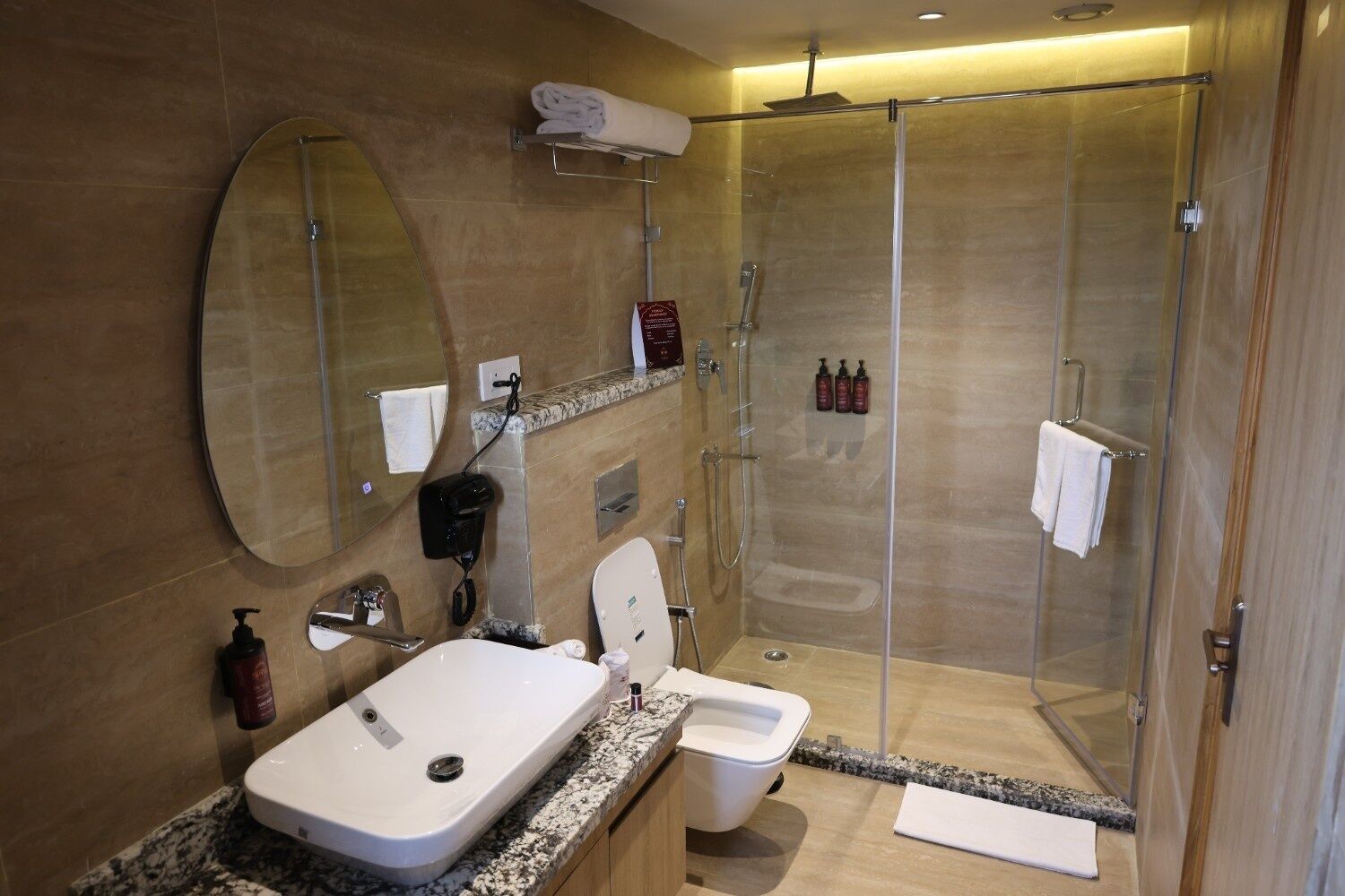 Un baño moderno con ducha envuelta en vidrio, un espejo grande, inodoro y lavabo con encimera de mármol.