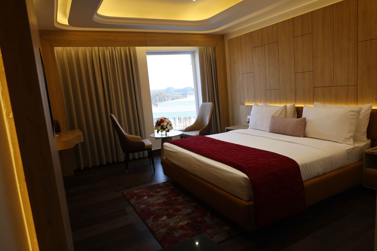 Habitación de hotel con una cama grande, un escritorio con silla, vista al mar y pared de paneles de madera.