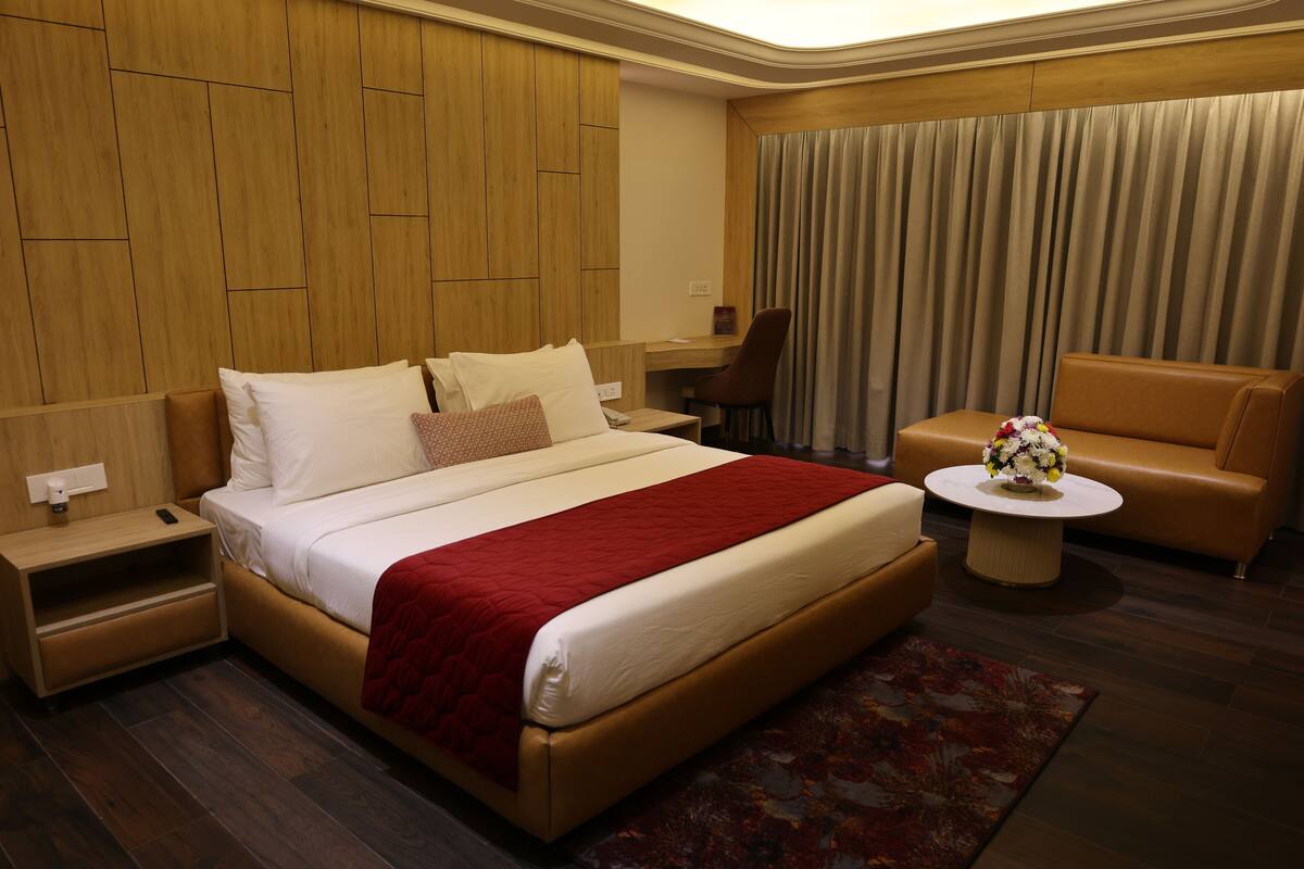 Habitación de hotel con una cama grande, un escritorio, una silla y una mesita con un jarrón de flores.