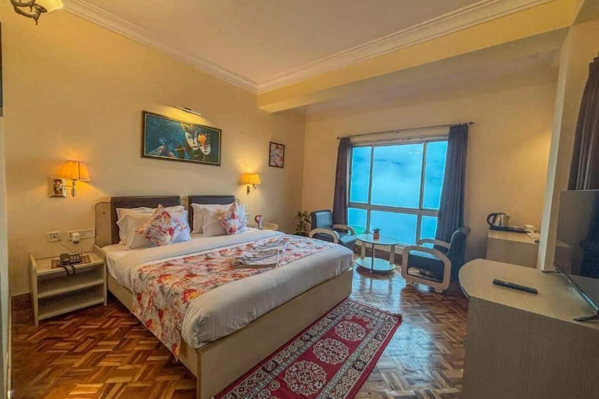 A hotel room with a large bed, a desk, a chair, a TV, and a window with curtains.
