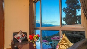 Ein Zimmer mit einem großen Fenster, einem Holztisch und zwei Sofas mit floralen Kissen.