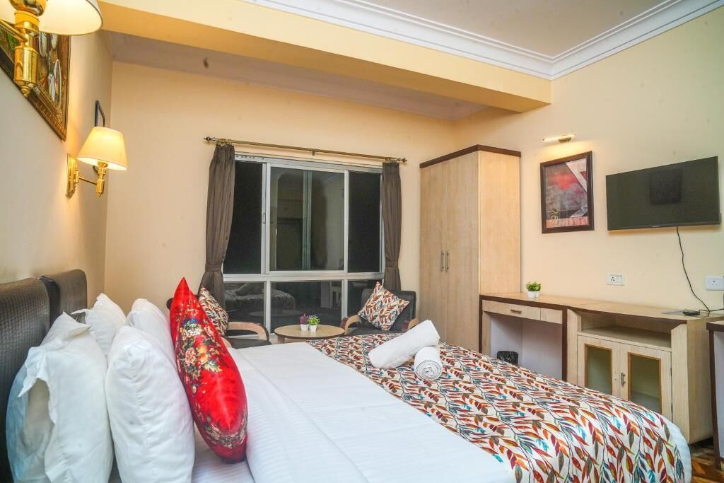 A hotel room with two beds, a desk, a chair, a TV, and a window with curtains.