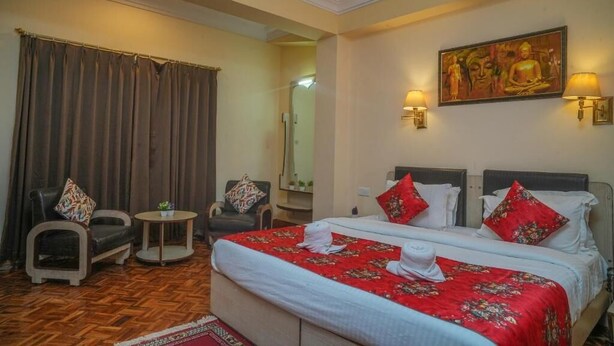 Une chambre d’hôtel avec deux lits, un coin salon comprenant une chaise et une petite table, et un tableau accroché au mur.