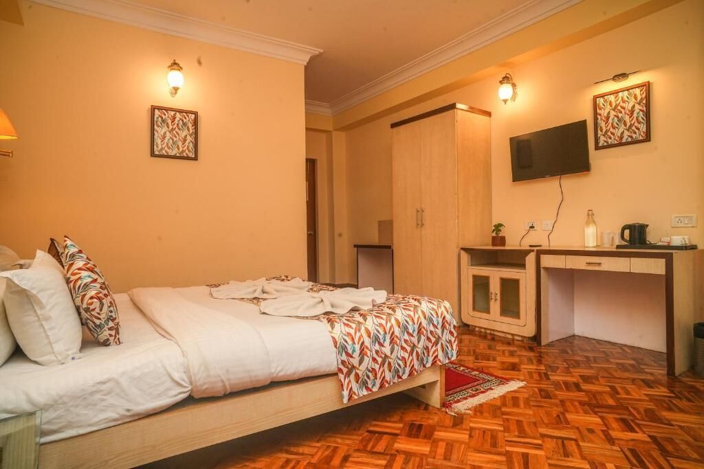 A bedroom with a bed, a desk, a wardrobe, and a television.