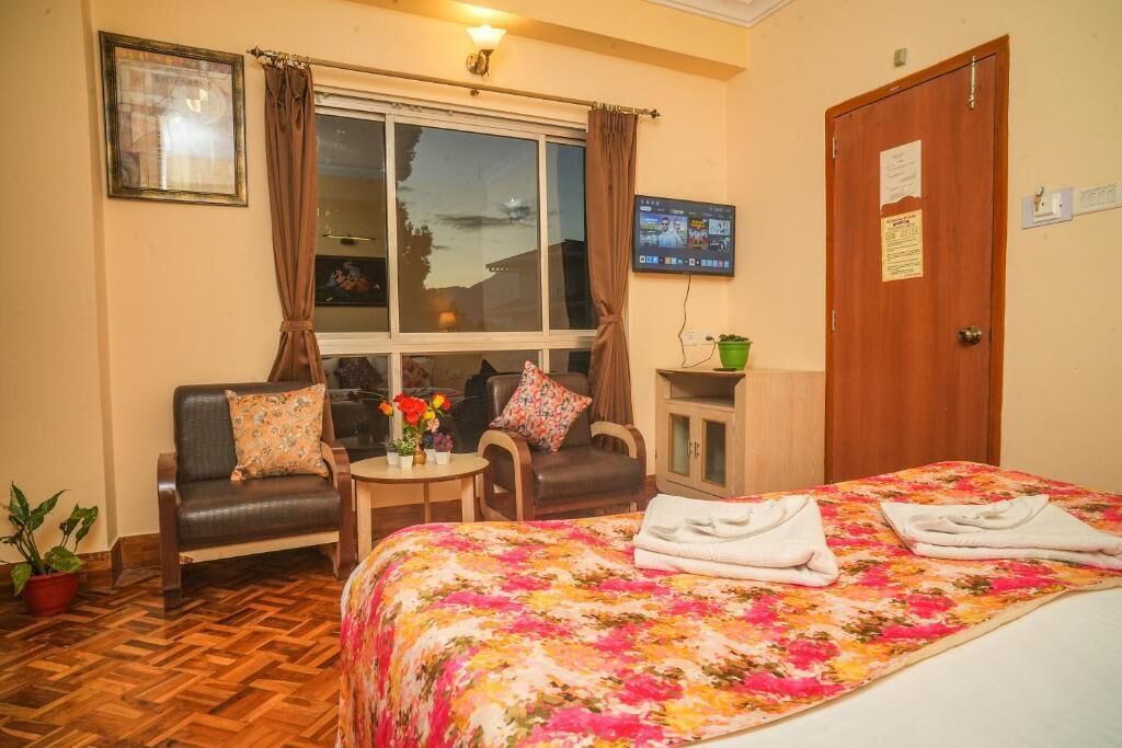 A hotel room with a bed, a sofa, a small table with flowers, a TV, and a door with a sign.