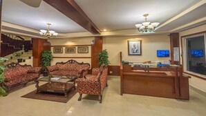 Eine Lobby mit einer Rezeption, zwei gestreiften Sofas, einem Couchtisch und einer Treppe im Hintergrund.