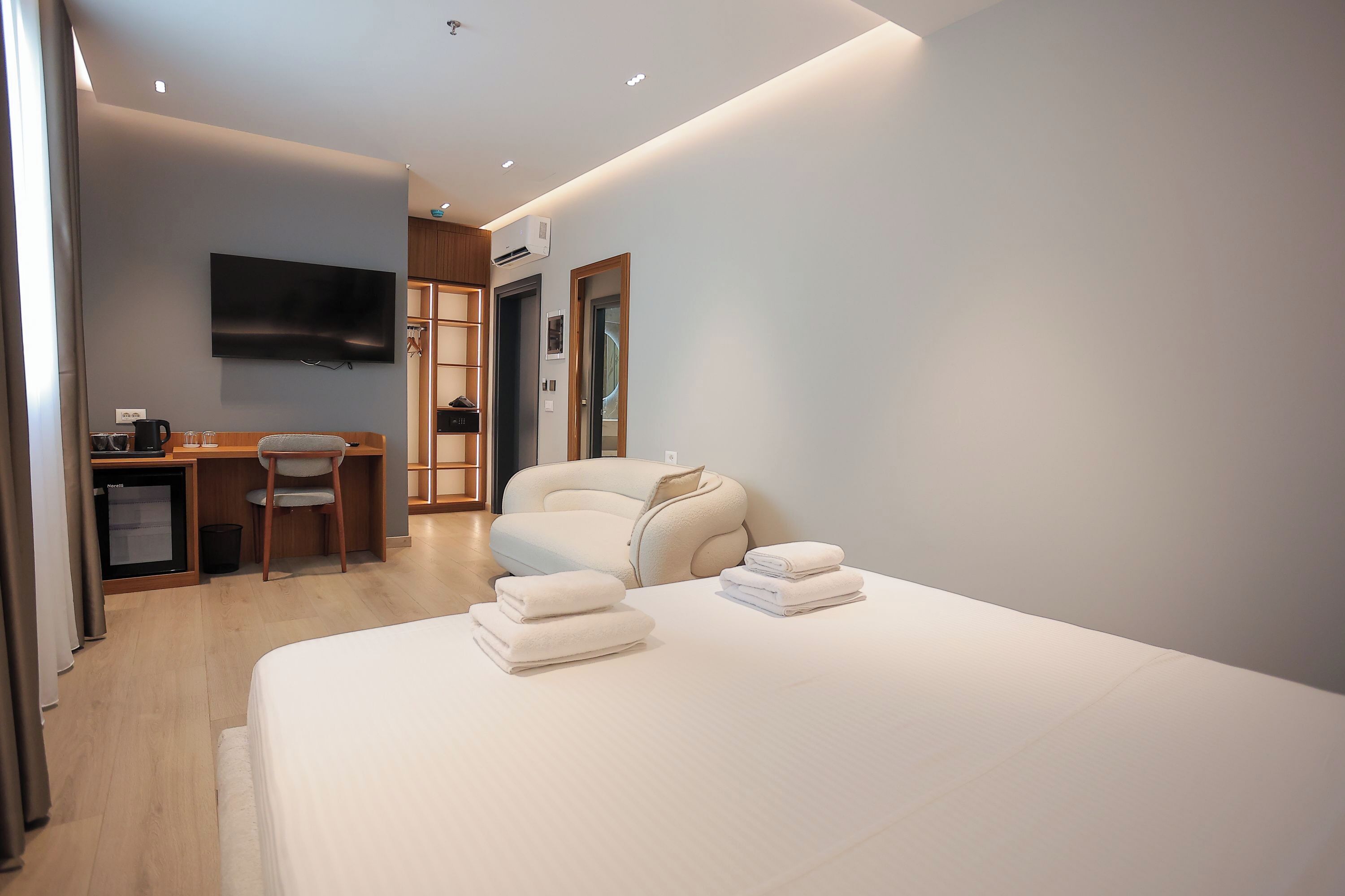 A modern hotel room with a bed, a desk with a chair, a television, and a wardrobe.