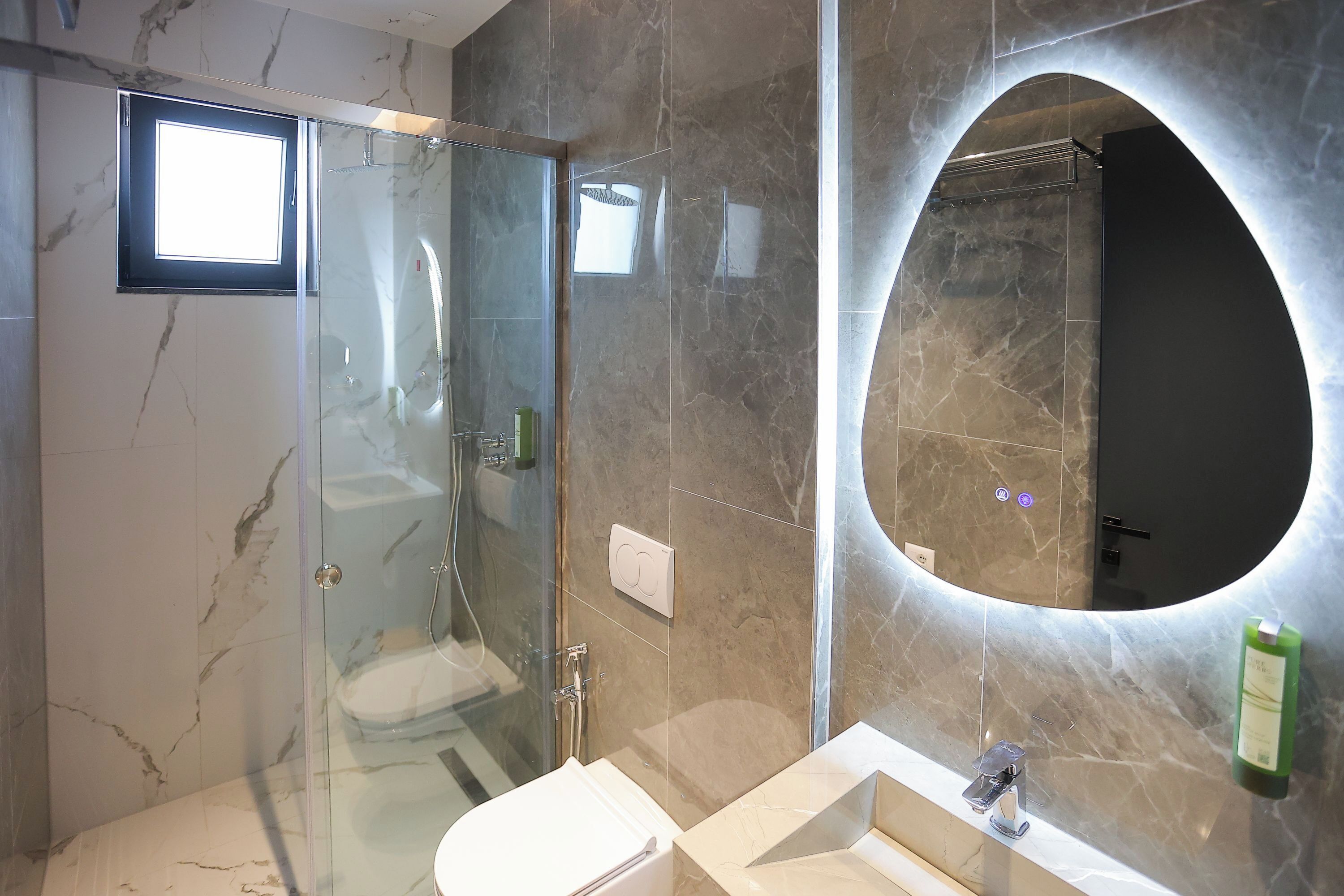 A modern bathroom with a glass shower enclosure, a vanity with a sink, and a large mirror with an arch above it.