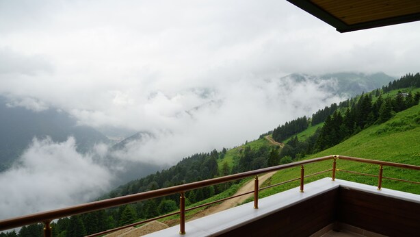 Un balcon offrant une vue sur un paysage montagneux, avec une balustrade en bois et un sol carrelé.