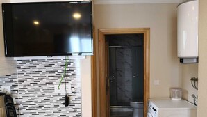 Une salle de bain compacte au design moderne, comprenant un mur recouvert de carreaux, un téléviseur fixé au mur, un lave-linge et des toilettes.
