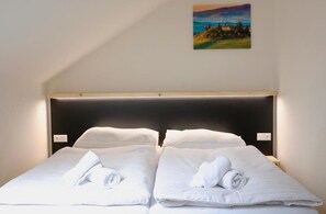 A double bed with white linens and towels, a dark headboard, and a painting of a landscape on the wall. - Penzion U Massima (Vyskov)