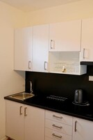A kitchen with white cabinets, a black countertop, a stainless steel sink, and a kettle.