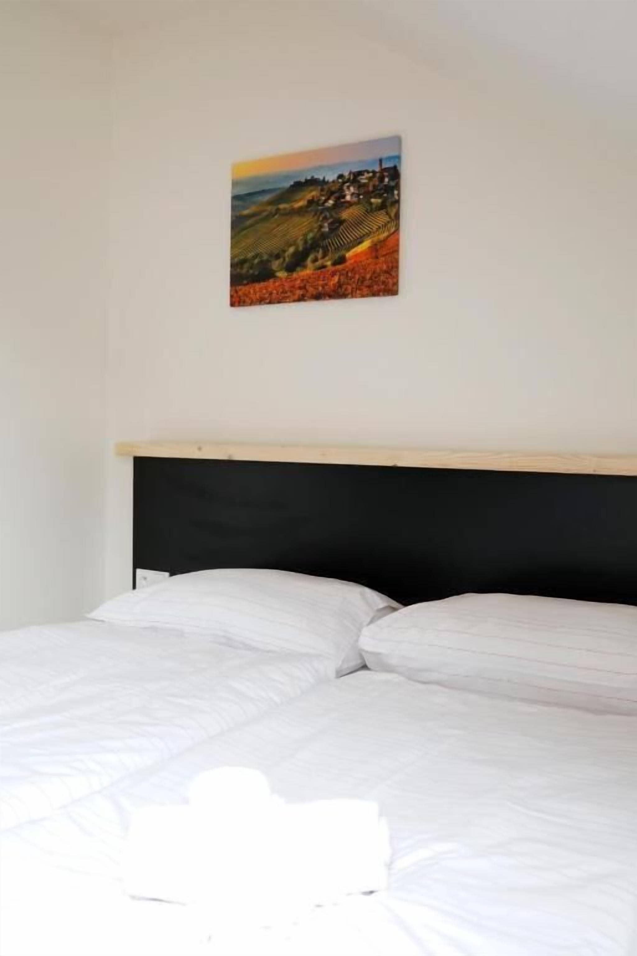 A bed with white bedding, a black headboard, and a landscape painting on the wall.