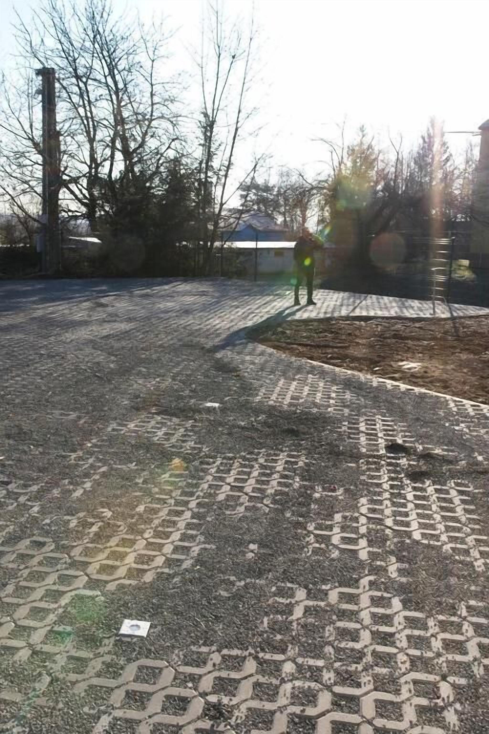 An outdoor area with a patterned pavement, a metal fence, and leafless trees.