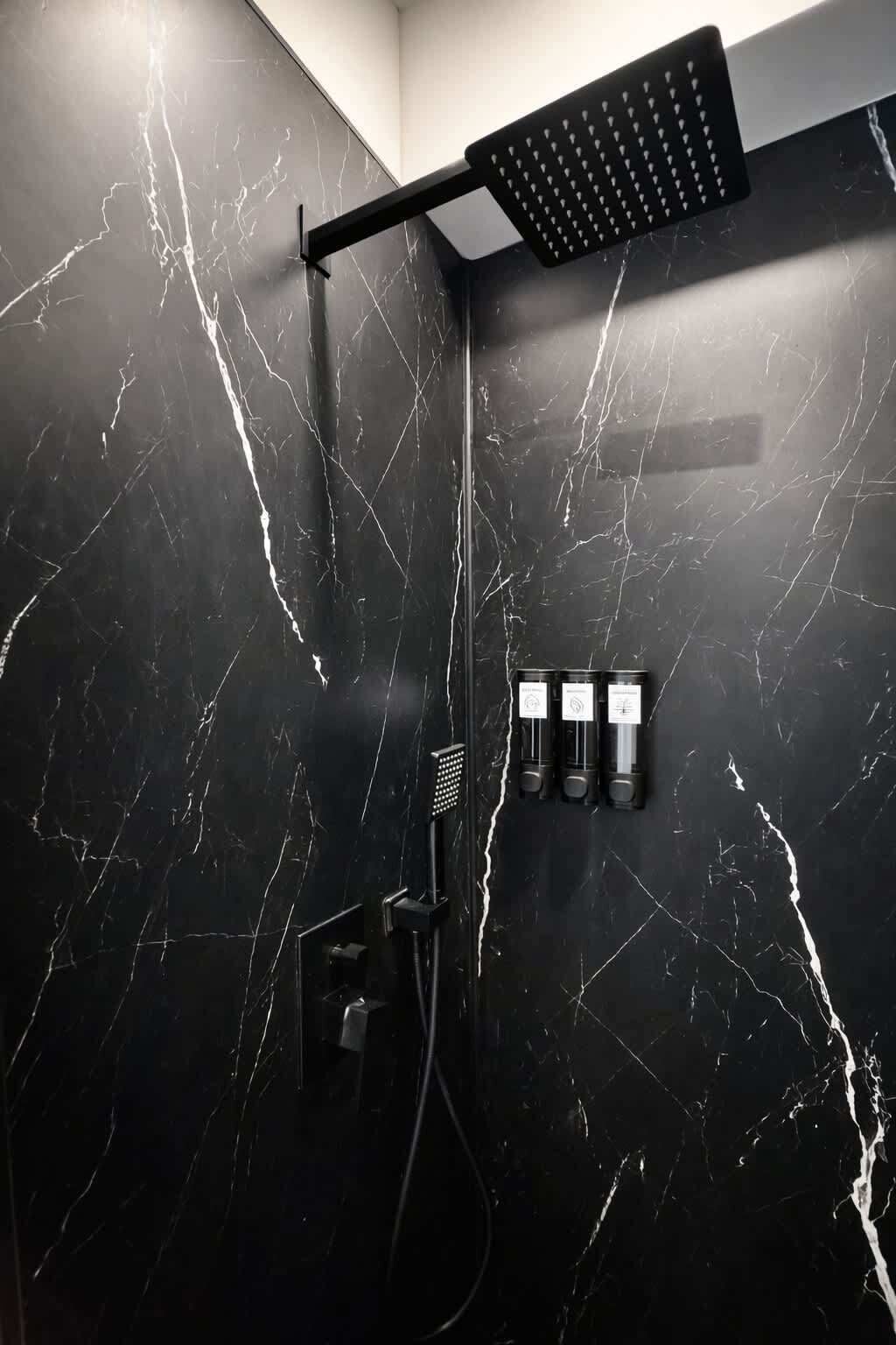 Een moderne badkamer met een wand van zwart marmer, een douchekop en drie flessen shampoo.