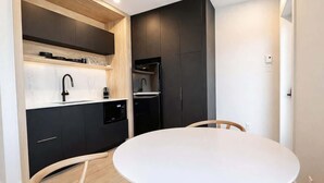 A modern kitchen with dark cabinetry, a white countertop, and a round dining table with wooden chairs. - Studio #7 - Steve Jobs | A/C • 5 min downtown (Québec City)