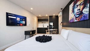 A hotel room with a bed, a TV displaying Philips Roku interface, a painting on the wall, and a kitchenette in the background. - Studio #6 - The Hendrix | A/C • 5 min downtown (Québec City)