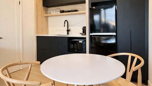 A modern kitchen with black cabinets, a white countertop, and a built-in microwave. There is a round white table with two wooden chairs. - Studio #6 - The Hendrix | A/C • 5 min downtown (Québec City)