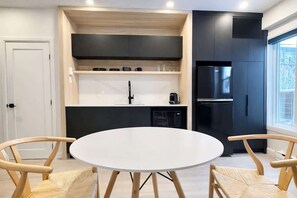 A modern kitchen with black cabinets, a white countertop, and a round table with chairs. - Studio #5 - The Monroe | A/C • 5 min downtown (Québec City)
