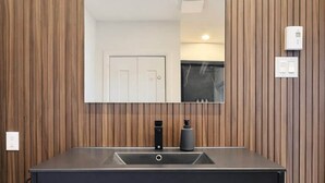 Een badkamer met een wand van houten panelen, een grote spiegel, een zwart wastafel en een kraan.