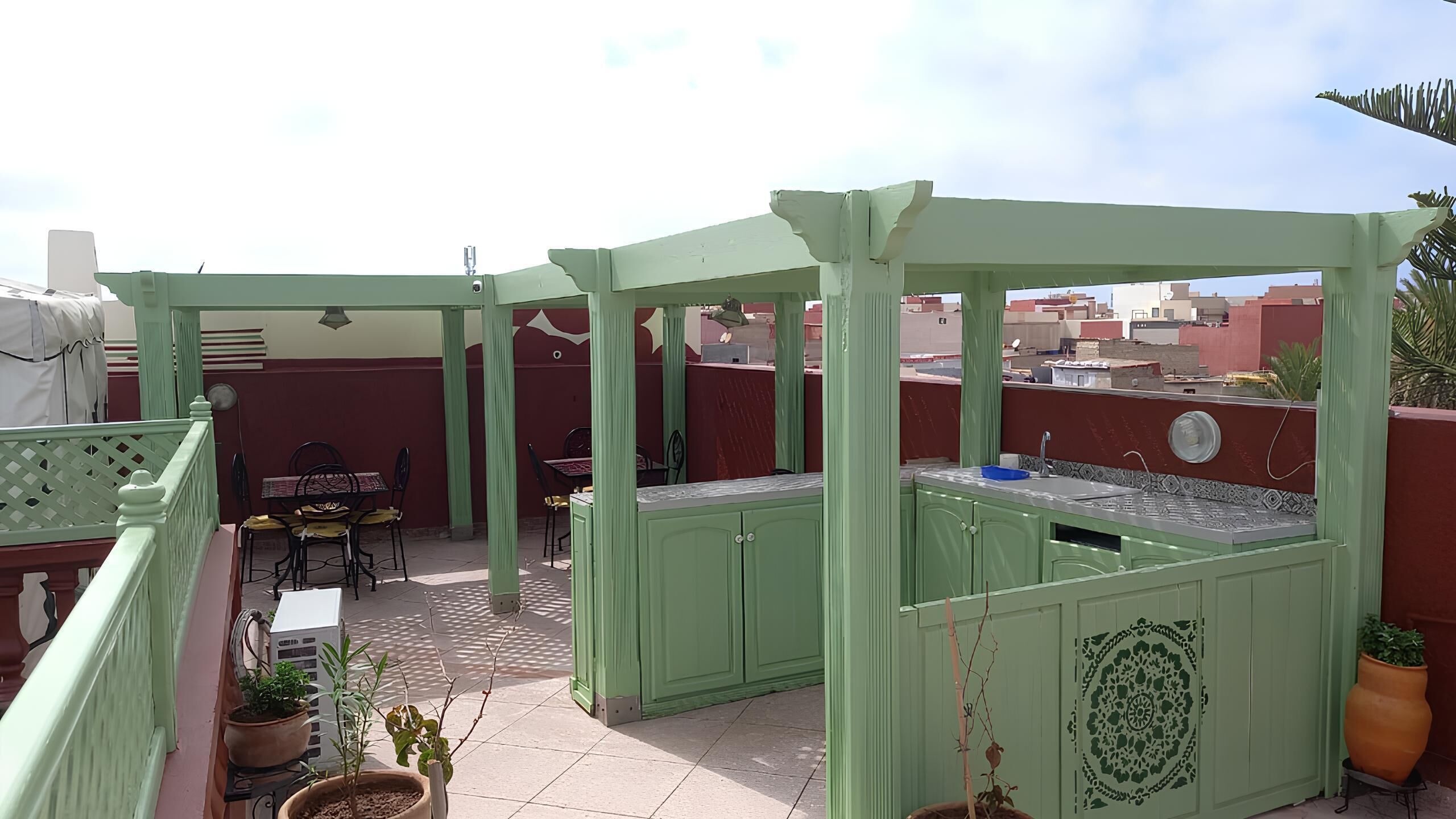 A rooftop patio with green furniture, a small kitchen area, and potted plants.