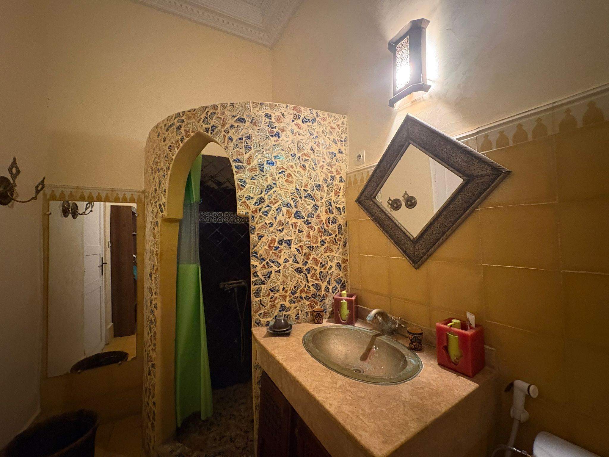 Een badkamer met een wand betegeld met mozaïek, een wastafel met spiegel en een groen gordijn.