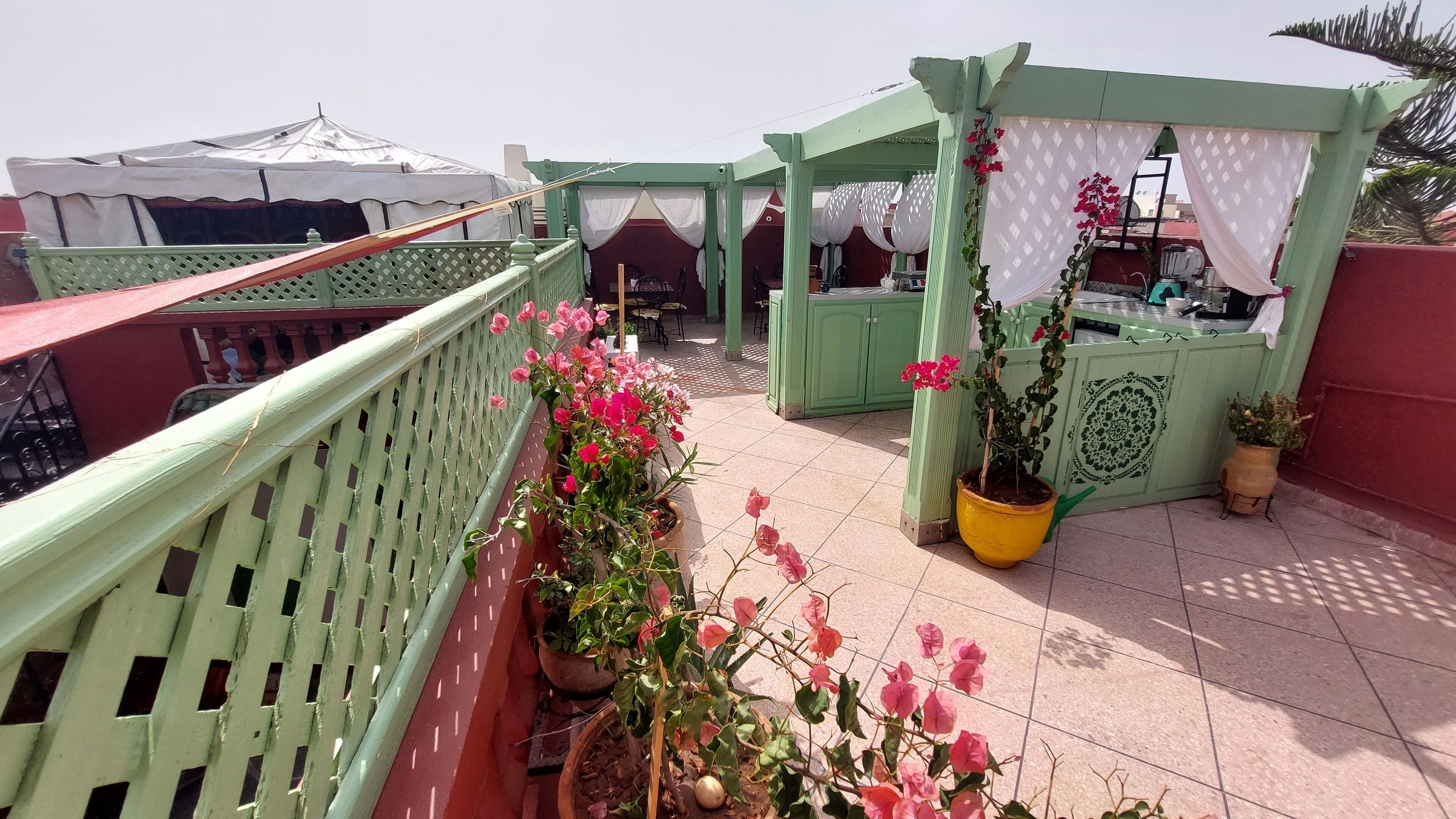 A rooftop terrace with a green railing, potted plants, and a covered seating area.